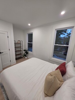 Ein Schlafzimmer mit Bett, Fenster, Tür und Regalelement.