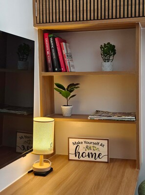 A wooden shelf with books, a potted plant, a lamp, and a sign that reads 'Make Yourself at home'. - Ground Floor Studio with Patio and Pool View at Casa Mira Towers, Mandaue (Mandaue)