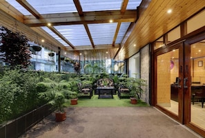 A covered outdoor area with a wooden ceiling, seating, and potted plants.