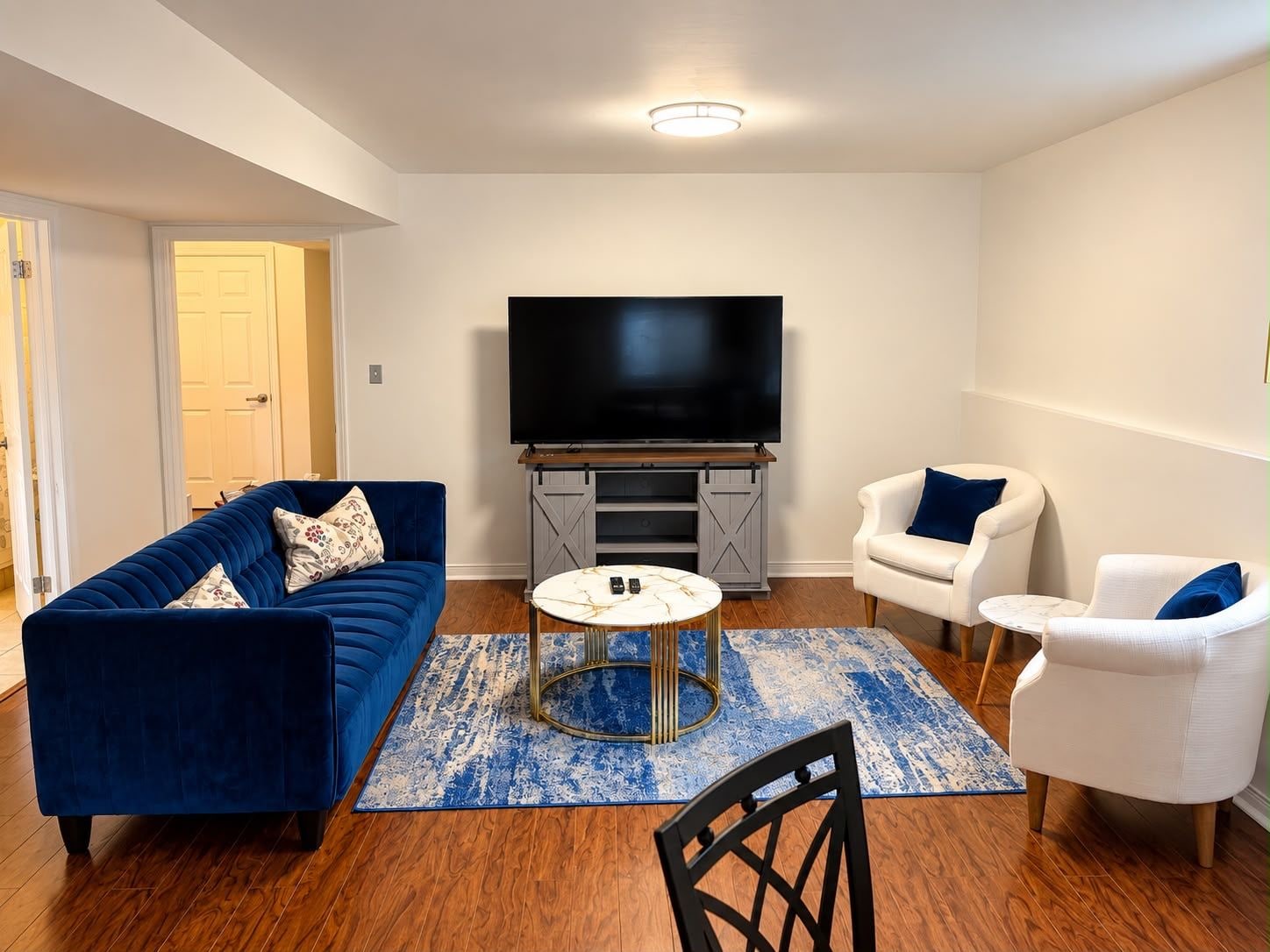 A living room with a blue sofa, white armchairs, a coffee table, and a flat-screen TV.