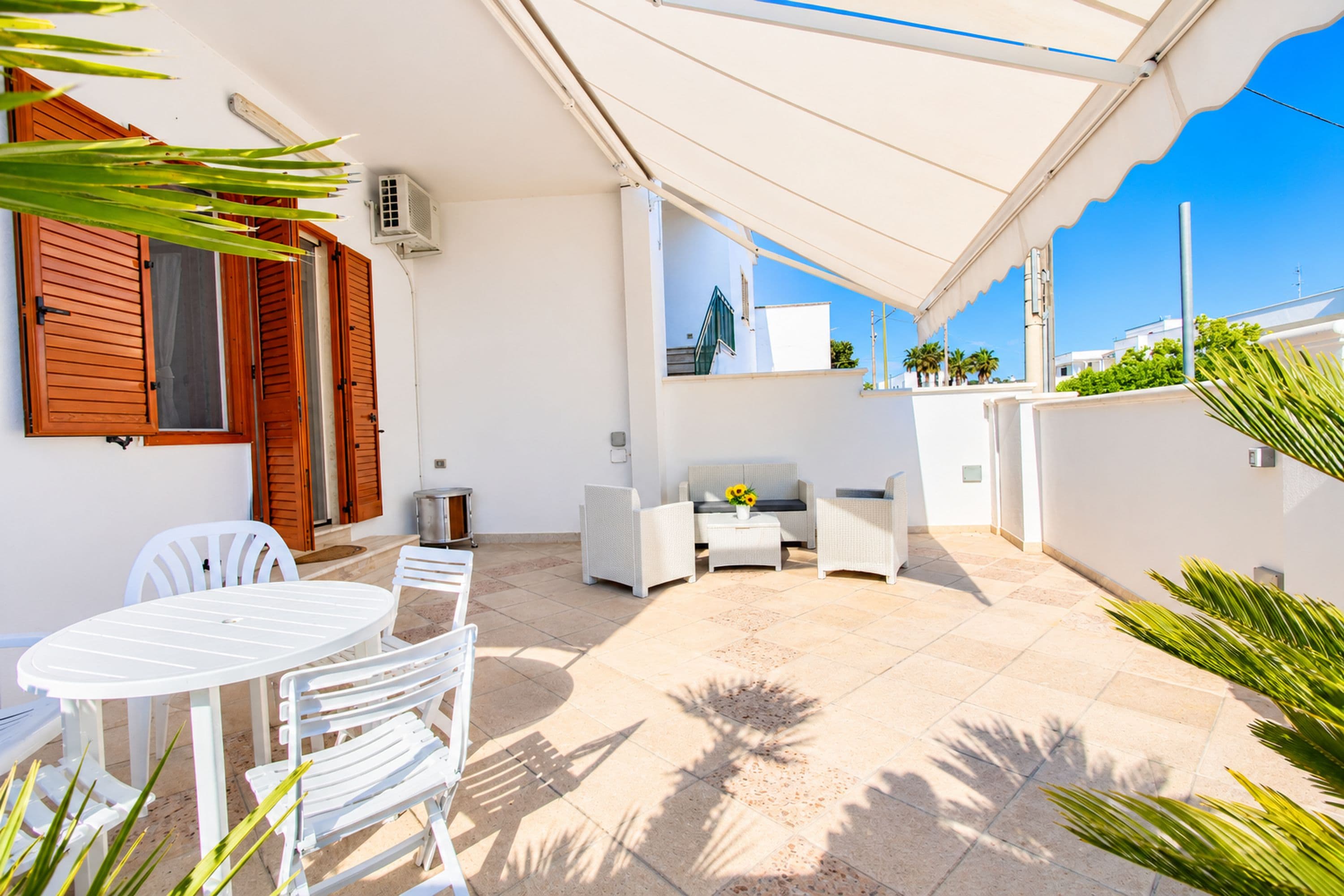 Un patio techado al aire libre con mobiliario blanco, una mesa y sillas.