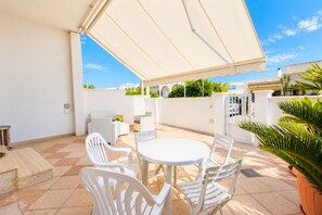 An outdoor patio with a round table and white chairs, a covered area, and a view of the surrounding buildings and greenery. - Apartment with a spacious outdoor area in the center of Santa Maria di Leuca (Santa Maria di Leuca)