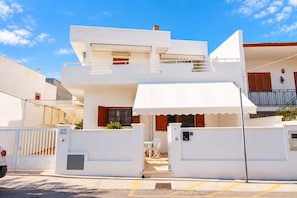 A two-story building with a white facade, a gated entrance, and a balcony with a metal railing. - Apartment with a spacious outdoor area in the center of Santa Maria di Leuca (Santa Maria di Leuca)