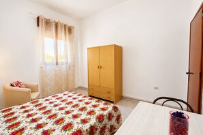 A bedroom with a bed, a wooden wardrobe, a chair, and a table. - Apartment with a spacious outdoor area in the center of Santa Maria di Leuca (Santa Maria di Leuca)