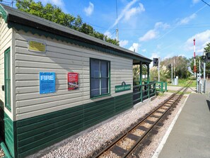 Ein kleiner Bahnhof mit einstöckigem Bau und grüner Dachbegrünung, eine Beschilderung für Videoüberwachung sowie mehrere Hinweisschilder zu Sicherheit und Informationen.