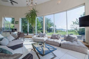 A spacious living room with a large window, a sofa set, a coffee table, and a television.