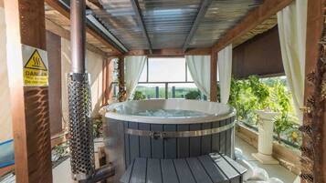 A hot tub in a covered outdoor area with a warning sign, a metal pipe, and a view of greenery.