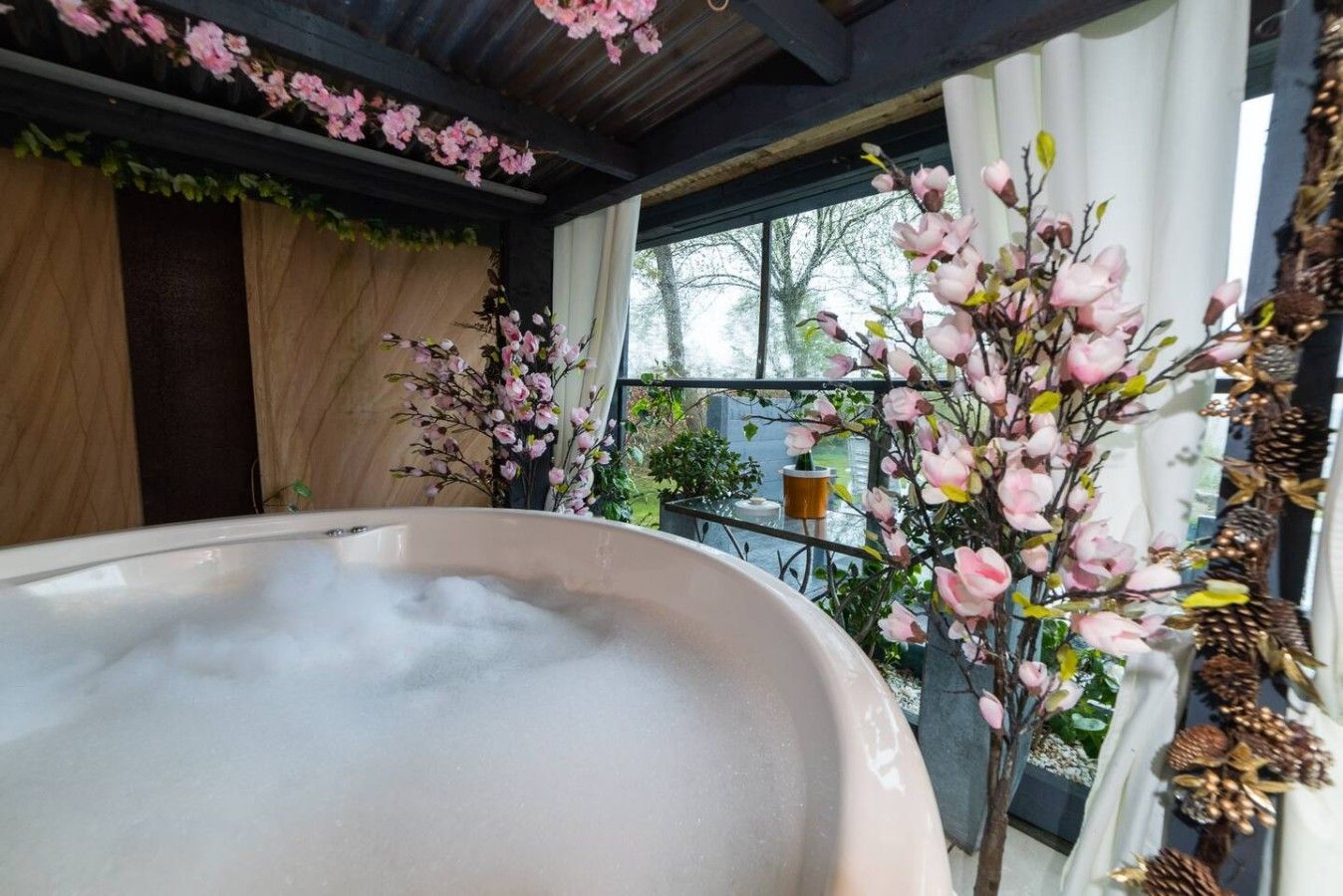 A hot tub in a covered outdoor area with a view of a garden and trees.