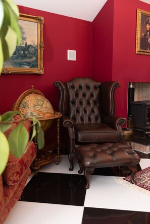 A room with a red wall, a large framed painting, a globe, a leather armchair, and a fireplace.