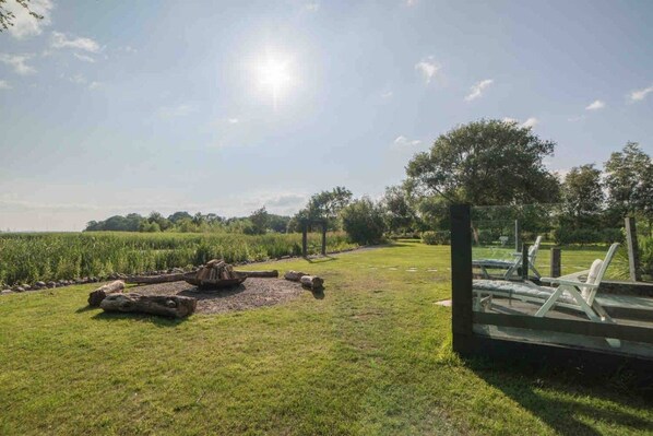An outdoor area with a grassy field, a wooden fire pit, and a seating area with chairs.