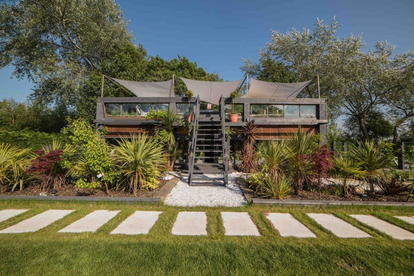 A modern two-story house with a central staircase, surrounded by a well-maintained garden with various plants and a gravel pathway.