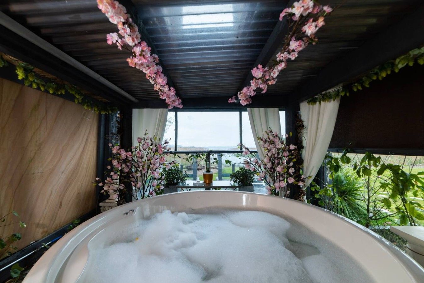A hot tub with a view of a garden and a building in the background.