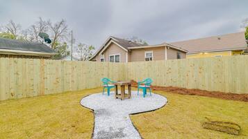 Un patio trasero con una mesa y sillas de madera, un sendero de grava y una cerca de madera.