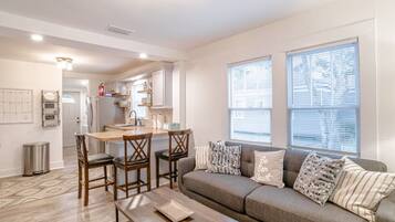 A modern living room with a sofa, a dining table with chairs, and a kitchen in the background.