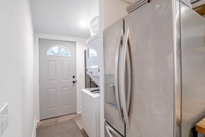 Un área de lavandería con lavadora y secadora, un refrigerador de acero inoxidable y una puerta blanca con ventanal.
