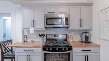 Una cocina con gabinetes blancos, un microondas de acero inoxidable, una estufa a gas y una cafetera.