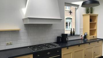 A modern kitchen with a gas stove, black countertop, beige cabinets, and a black pendant light.