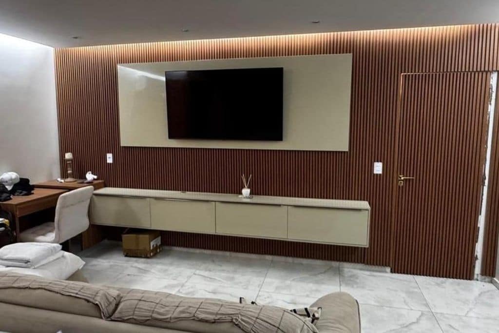 Een moderne kamer met een flatscreen televisie aan de muur, een bank, een bureau met stoel en een kastje onder de televisie.