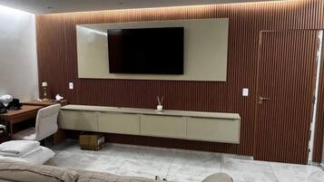 Een moderne kamer met een flatscreen televisie aan de muur, een bank, een bureau met stoel en een kastje onder de televisie.