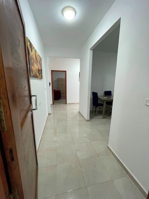 A hallway with a tiled floor, a wooden door, and a dining area with chairs and a table. - Dar Kmar Djerba Midoun  (Djerba Midun)