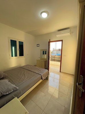 A bedroom with a bed, a dresser, a mirror, and a door leading to an outdoor area. - Dar Kmar Djerba Midoun  (Djerba Midun)