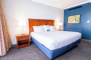Habitación de hotel con una cama grande, dos mesitas de noche con lámparas, una pared azul y un cuadro.