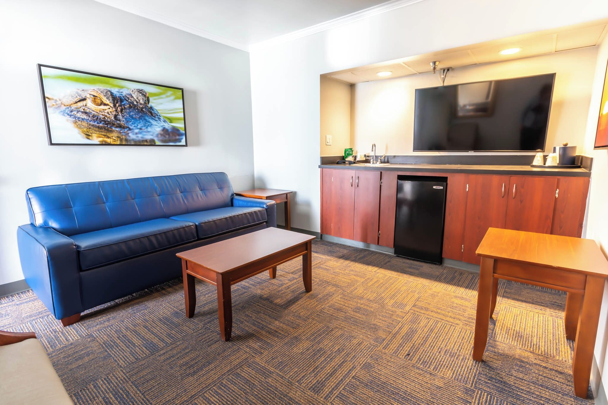 A living room with a blue sofa, a wooden coffee table, and a kitchen area with a large TV and cabinets.