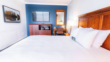 Ein Hotelzimmer mit einem großen Bett, einem Schreibtisch mit Stuhl, einem Fernseher, einem Spiegel und einem Fenster.