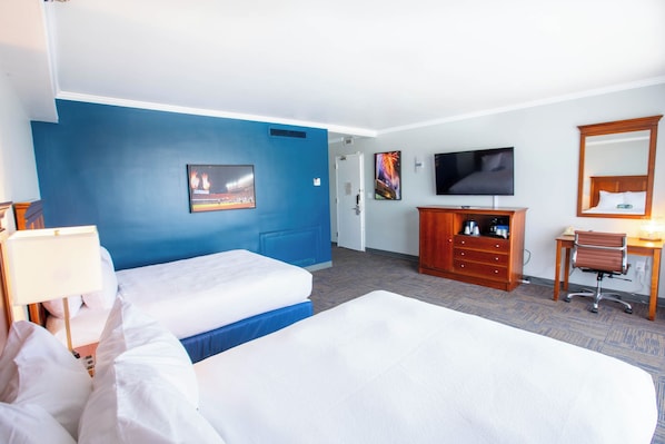 A hotel room with two beds, a TV, a desk with a chair, and a dresser.