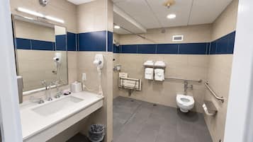A modern bathroom with a dual sink vanity, a mirror, a hair dryer, a toilet, and a trash bin.