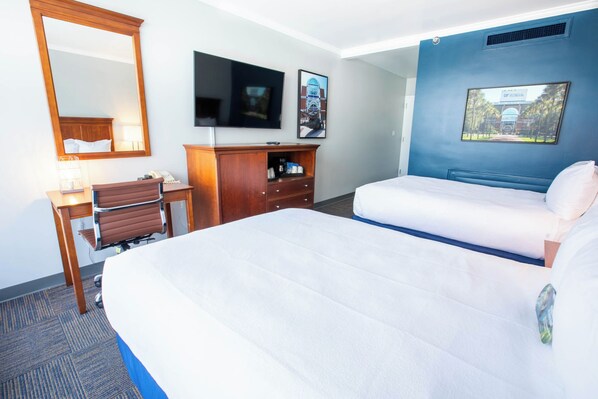 A hotel room with a large bed, a desk with a chair, a television, and a framed picture on the wall.