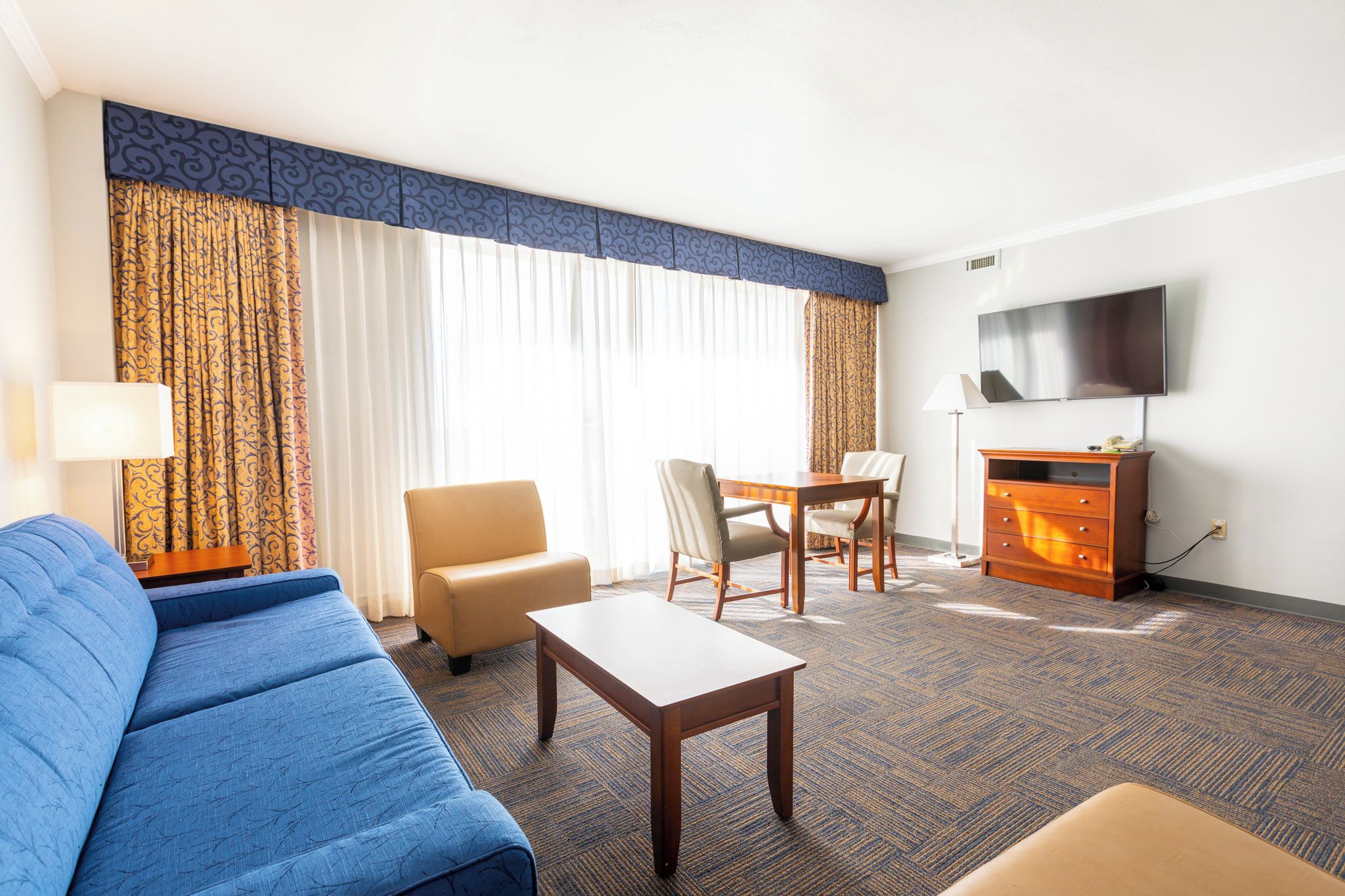 A hotel room with a sofa, a small table, a chair, a TV, and a cabinet.