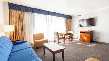 A hotel room with a sofa, a small table, a chair, a TV, and a cabinet.
