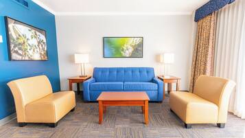 Ein Hotelzimmer mit einem blauen Sofa, zwei Sesseln, einem Holztisch und zwei Nachttischen mit Lampen.