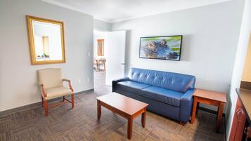Ein Zimmer mit einem blauen Sofa, einem Holzstuhl, einem kleinen Tisch, einem Spiegel und einem Bild von einem Tier.