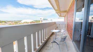 Een balkon met een tafel, stoelen, een glazen deur en uitzicht op gebouwen en een koepel.