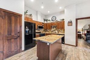 Una cocina con armarios de madera, un refrigerador negro, una encimera de mármol y un reloj en la pared.