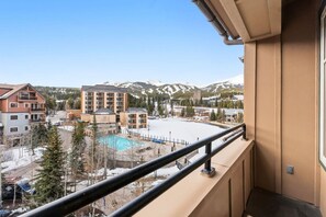 A view from a balcony overlooking a swimming pool, buildings, and snow-capped mountains. - 3 bedroom Main Street Station Ski-in/out & Hot Tub (Breckenridge)
