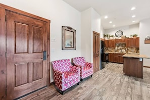 A hallway with a wooden door, a patterned sofa, a mirror, and a kitchen area with wooden cabinets and a marble countertop. - 3 bedroom Main Street Station Ski-in/out & Hot Tub (Breckenridge)