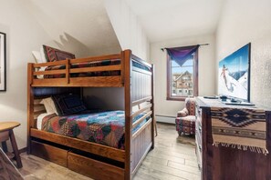 Quarto aconchegante com uma cama beliche, uma escrivaninha com computador e uma janela com vista para prédios.