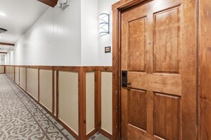 Um corredor com painéis de madeira, carpete estampado e porta de madeira com puxador.