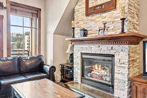 A living room with a stone fireplace, leather sofa, and a coffee table. - 3 bedroom Main Street Station Ski-in/out & Hot Tub (Breckenridge)