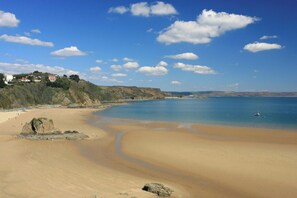 Ein Strand mit blauem Himmel, ruhigem Wasser und wenigen Personen.