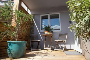Ein kleiner Innenhof mit einem Holztisch und zwei Stühlen, einem Topfpflanzen und einem Fenster mit Jalousien.