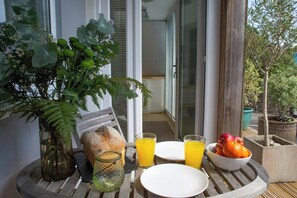 Ein Frühstückstisch mit Brot, zwei Orangensaftgläsern, einer Obstschale und einem Blumentopf.