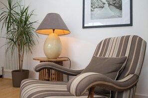 A striped armchair with a cushion, a lamp on a small table, a potted plant, and a framed picture on the wall. - The Gallery, Tenby - Two Bedroom Cottage, Sleeps 4 (Tenby)