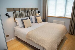 A bedroom with a bed, bedside lamps, a window with curtains, and a radiator. - The Gallery, Tenby - Two Bedroom Cottage, Sleeps 4 (Tenby)