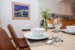 A dining table set with white bowls, wine glasses, and cutlery, with a painting and a vase of flowers on the wall. - The Gallery, Tenby - Two Bedroom Cottage, Sleeps 4 (Tenby)