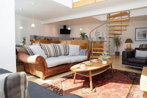 A modern living room with a sofa, a coffee table, and a staircase. - The Gallery, Tenby - Two Bedroom Cottage, Sleeps 4 (Tenby)