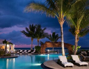 A pool area with lounge chairs, palm trees, and a rock formation. - ★★★★★ Golden Horizon Luxury Beach Studio (Sunny Isles Beach)